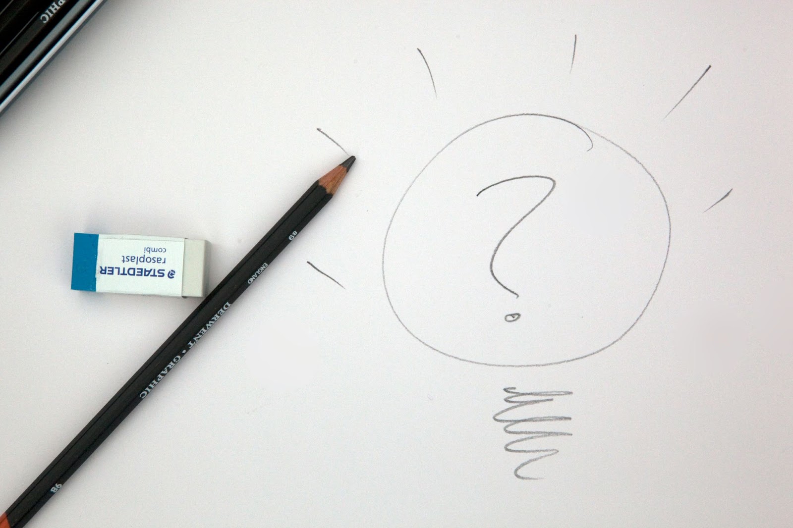 A pencil, an eraser, and a hand-drawn question mark in a lightbulb shape on white paper, suggesting a moment of brainstorming or problem-solving.