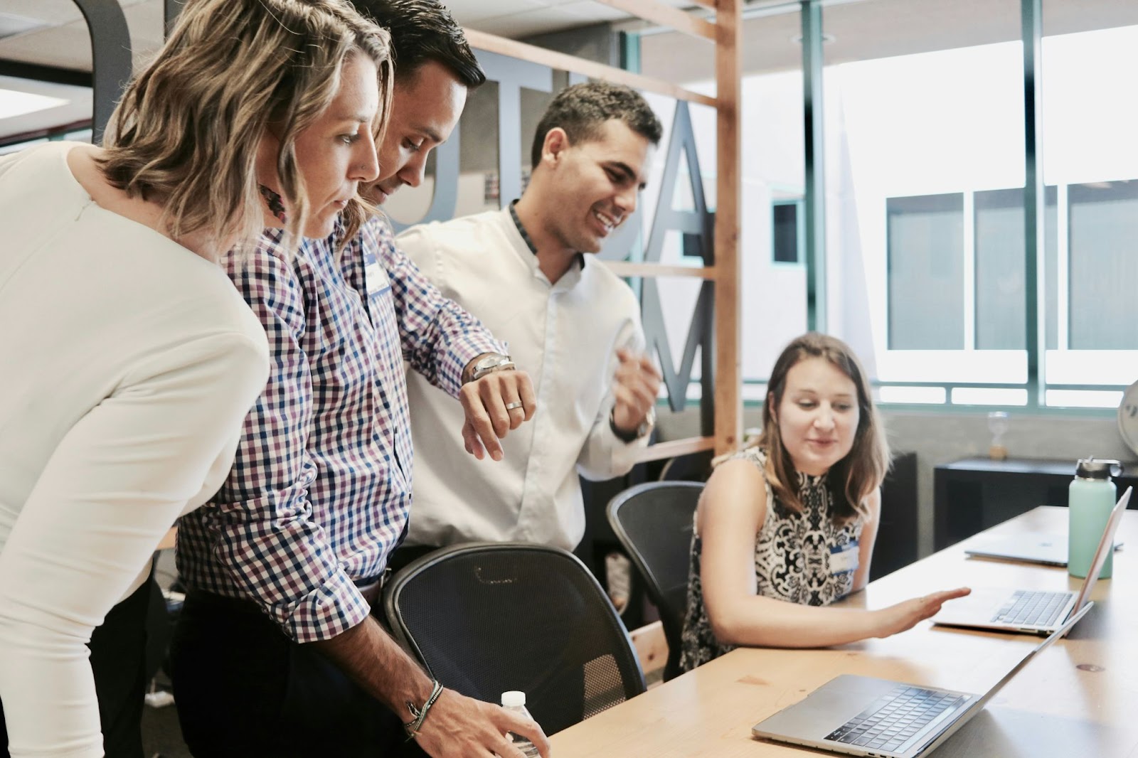 Group of professionals gathered around a desk, engaged in discussion while looking at laptops in a contemporary workspace.