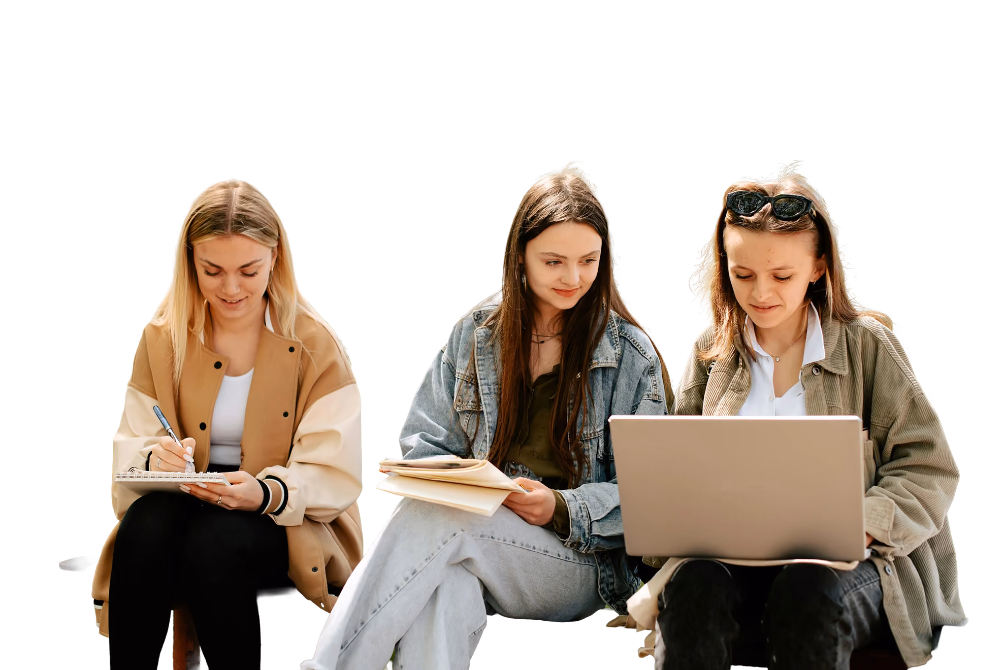 Three young women studying outdoors on a bench with notebooks and a laptop under trees.