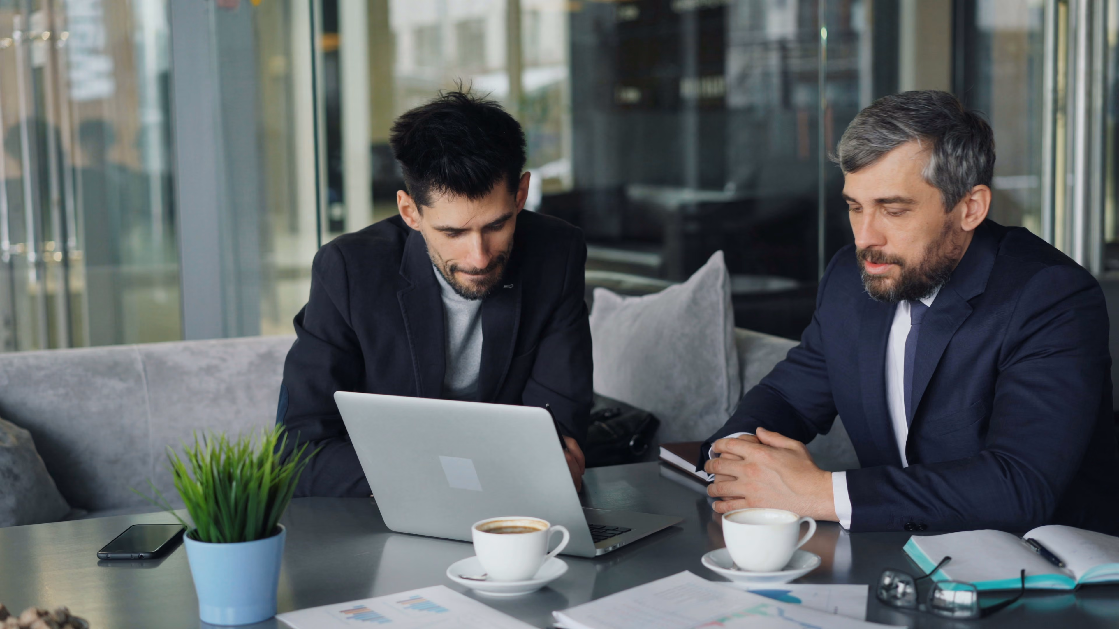 Three business people discussing charts and notes at a table with coffee cups and a laptop.