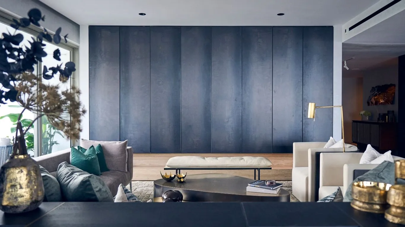 Modern living room with gray and beige sofas, green cushions, gold decor, and a wooden panel wall.