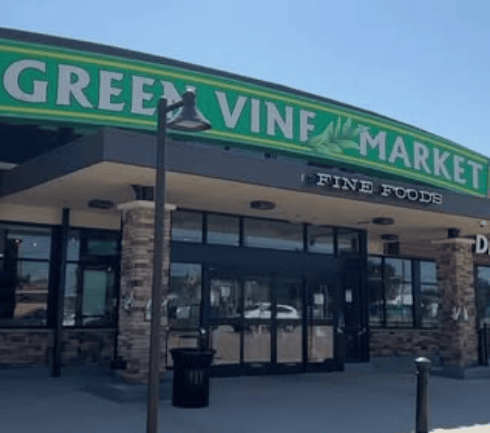 Entrance of Green Vine Market featuring a sign that reads "Fine Foods," with brick accents and large windows.