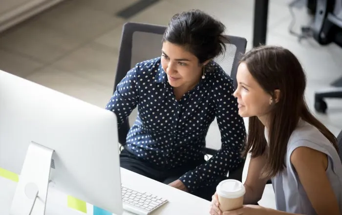 Two female employees sitting behind the same desk looking at a computer screen