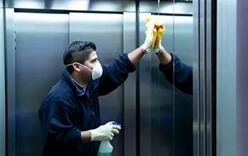 man cleaning an elevator with a facemask and heavy gloves, staring at his reflection