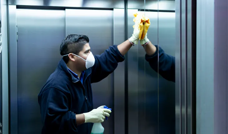 man cleaning an elevator with a facemask and heavy gloves, staring at his reflection