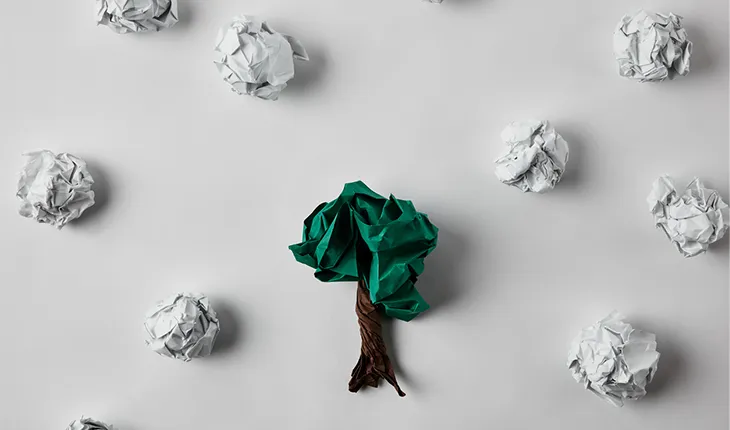 scrunched up peices of paper surround a peice of paper in the centre that has been coloured to look like a tree, whereas the others are white