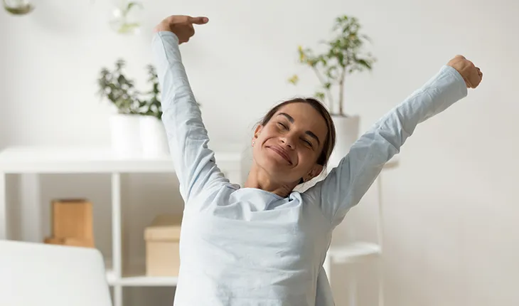 a young woman stretches up with a satisfied look, sitting in bright facilities fostering wellbeing