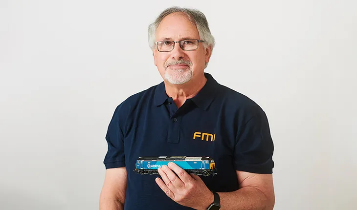 tim ireland, senior facilities management consultant, smiles at the camera, holding a model train