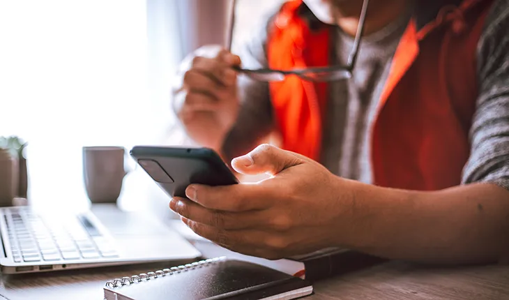 a facilities manager looks at their phone in front of an open laptop