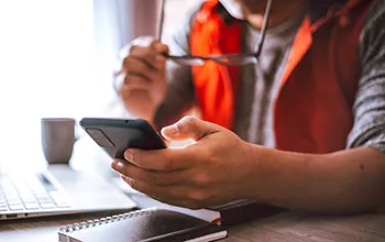 a facilities manager looks at their phone in front of an open laptop