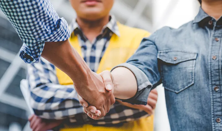 a facilities managers hakes hands with a contractor while a safety officer waits in the background.