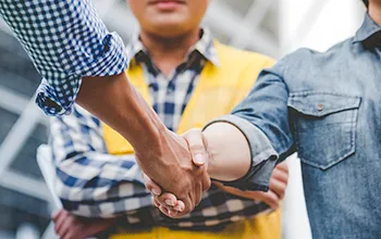 a facilities managers hakes hands with a contractor while a safety officer waits in the background.