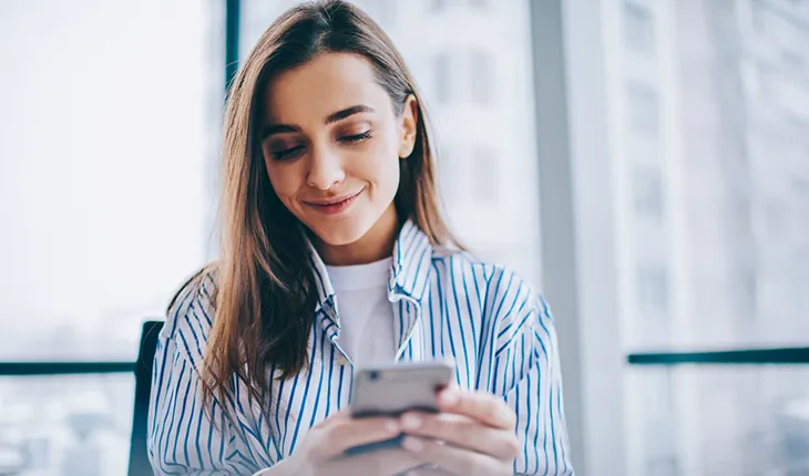 A young female facility user in a striped blue and white collared shirt smiles as she reads a notification.