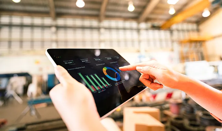 Hands hold an tablet device which is showing graphical data representations.