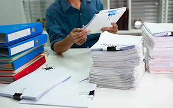 A professional in a navy button up shirt sorts through piles of paper and folders