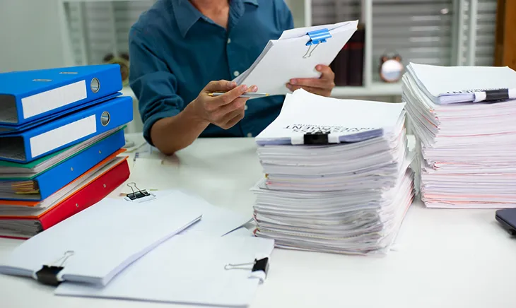 A professional in a navy button up shirt sorts through piles of paper and folders