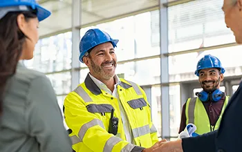 A facilities manager shakes hands with a contractor who is wearing a yellow high vis jacket and a blue hard har