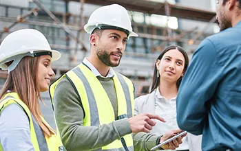 Two contractors wearing high vis discuss with two facilities managers while adding licence details to an ipad
