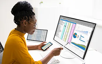 A young woman compares data on a computer with data on a phone screen