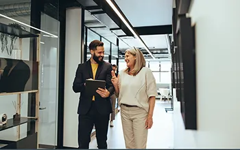 two colleaugues laugh during a friendly discussion walking down a hallway with an ipad