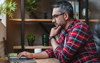A middle aged facilities manager inspects the screen of an open laptop