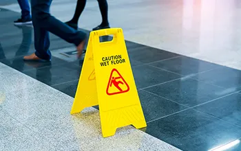 A yellow sign on dark blue tiles reading "caution wet floor" with an illustration of a person slipping