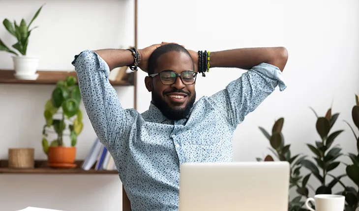 A facilites manager in a blue pattered shirt relaxes back in his chair, putting his hands behind his head
