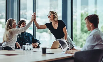 A group of faciliites managers celebrate around a table, high fiving and smiling