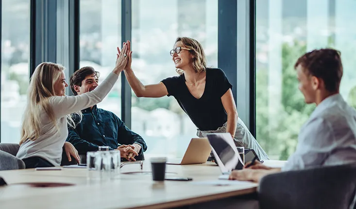 A group of faciliites managers celebrate around a table, high fiving and smiling