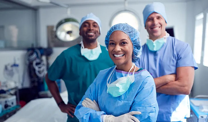 Three surgical staff smile at the camera from a clean operating theatre