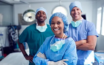 Three surgical staff smile at the camera from a clean operating theatre