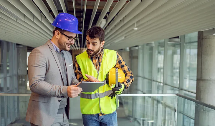 A facilities manager and a contractor look at an ipad discussing something and smile