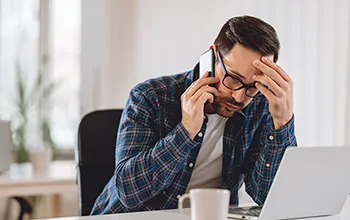 A facilities manager speaks on the phone in front of a laptop looking stressed