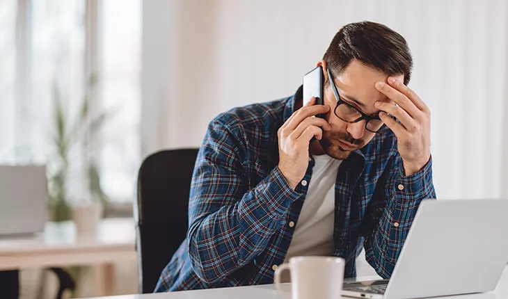 A facilities manager speaks on the phone in front of a laptop looking stressed