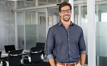 A facilities manager stands casually with hands in pockets, smiling at the camera