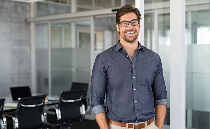 A facilities manager stands casually with hands in pockets, smiling at the camera
