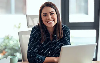 A facilities manager smiles at the camera from behind an open laptop