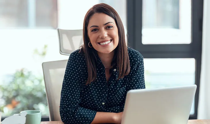 A facilities manager smiles at the camera from behind an open laptop