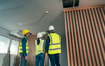 three facilities team members take a photo of a smoke detector on a tablet, to complete a condition assessment