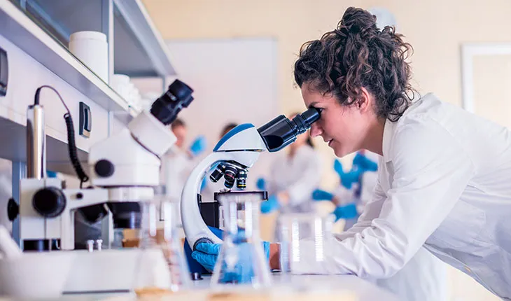 A scientist in a lab coat looks through a microscope in a laboratory. 
