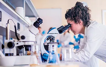 A scientist in a lab coat looks through a microscope in a laboratory. 