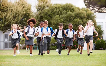 A group of primary school children run across a green oval towards the camera