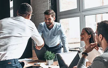 A facilities manager shakes the hand of a stakeholder in a white button up during a meeting