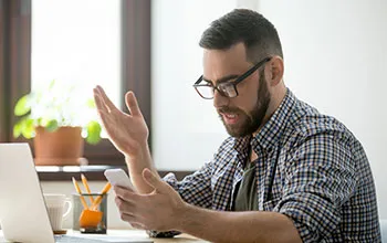 A facilities manager throws a hand up in exasperation while looking at a mobile phone