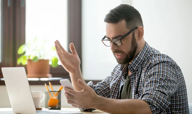 A facilities manager throws a hand up in exasperation while looking at a mobile phone