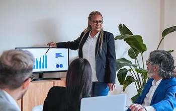 A facilities manager presents to management with the support of visual graphs shown on a monitor. 