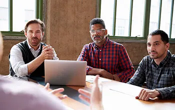 A group of culturally divserse facilities managers come together to listen to someone out of sight presenting to them.