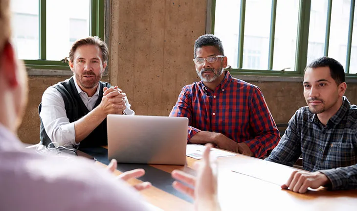 A group of culturally divserse facilities managers come together to listen to someone out of sight presenting to them.