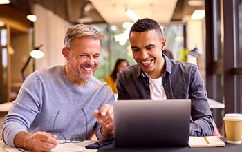 two facilities managers smile as they look at something on a laptop and share information