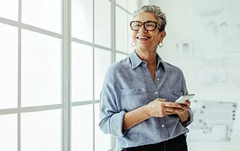 A, older, female facilities user smiles up from her phone in a brightly lit, mostly white office environment.